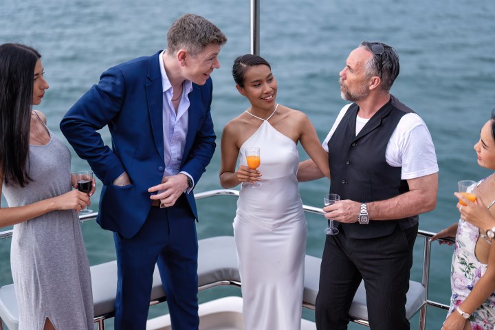 Group of people socializing on a boat, holding drinks and smiling.