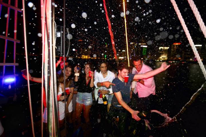 People celebrating on a boat at night with drinks and lights in the background.