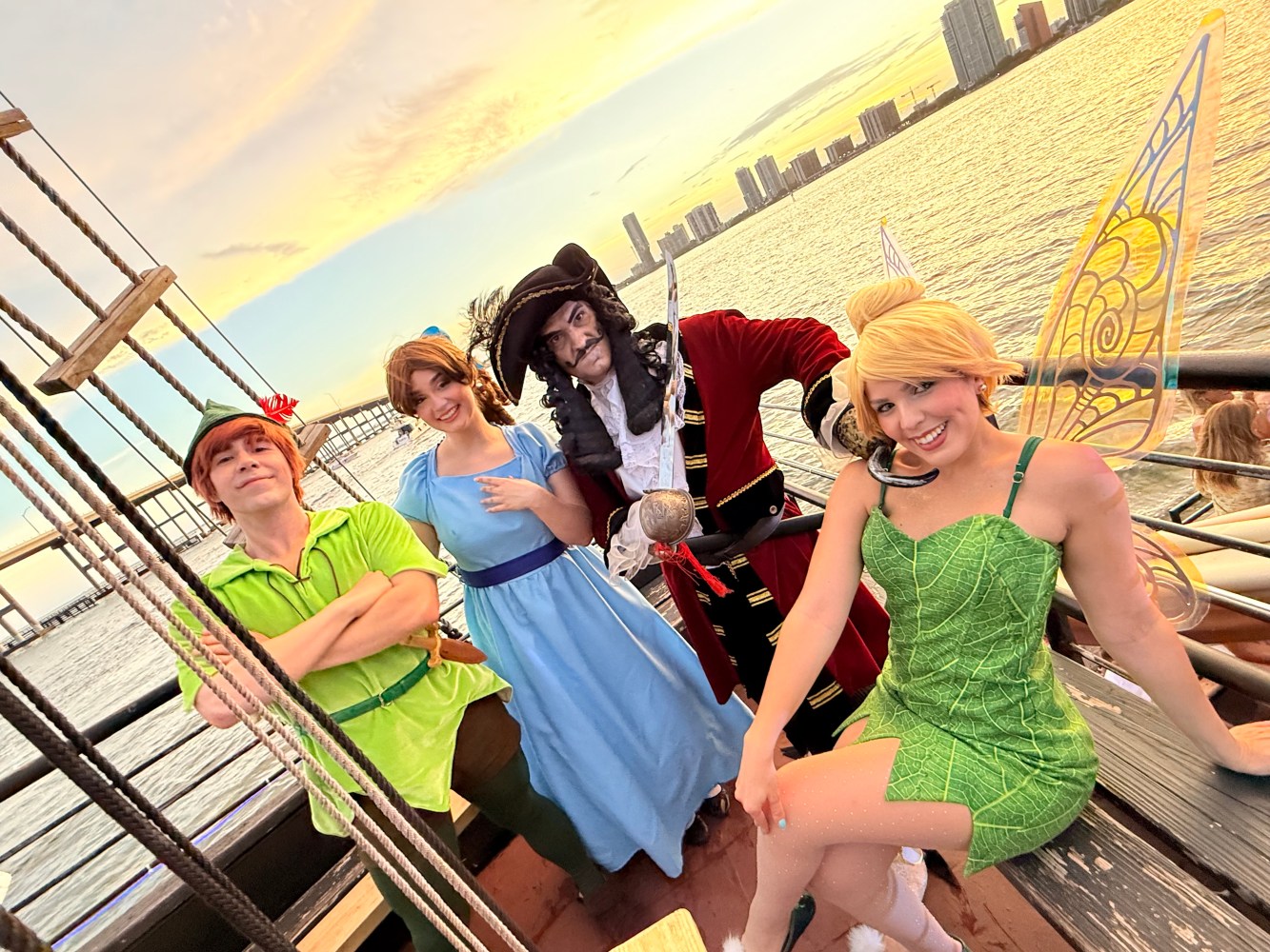 Four people in Peter Pan costumes on a ship deck at sunset.
