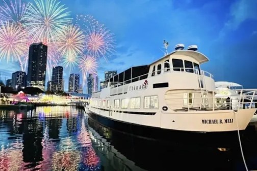 A boat docked at a marina with fireworks over a city skyline in the background.