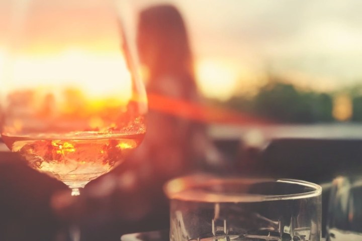A glass of wine and a sunset in the background with a blurred figure.