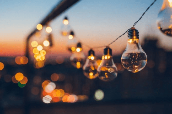 String of light bulbs hanging at sunset with city lights in the background.