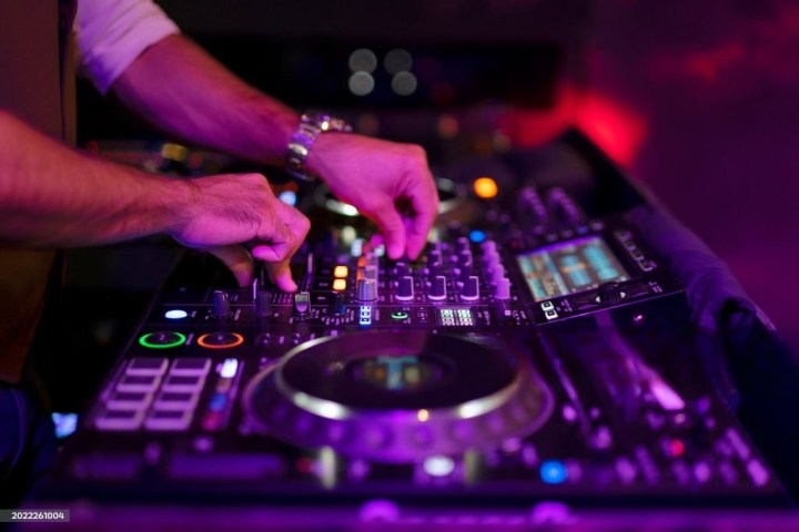DJ adjusting controls on a mixing console with colorful lights.