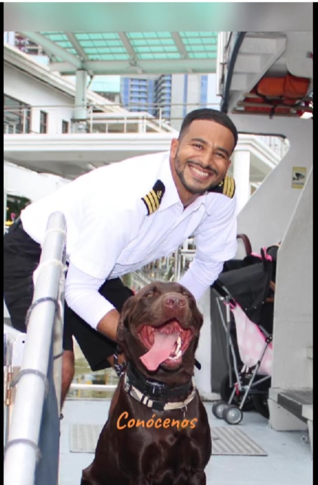 Man in uniform smiling with a dog on a docked boat, text 'Conócenos' on dog.
