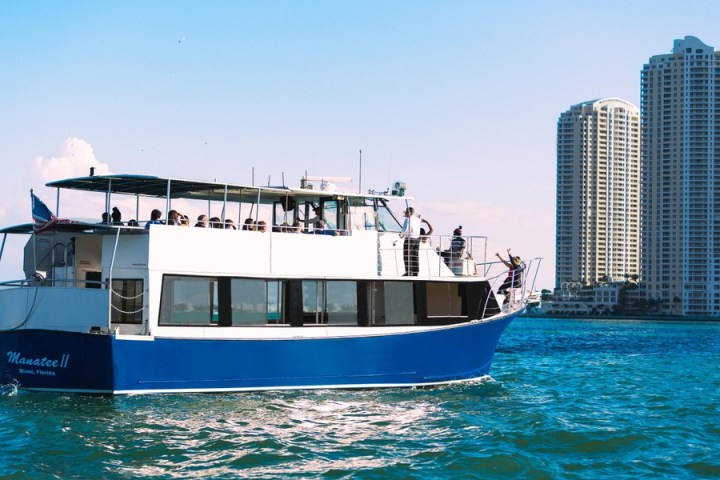 Tour boat 'Manatee II' on water with high-rise buildings in the background under a clear blue sky.