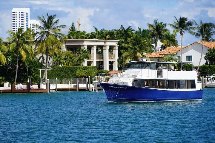 A blue and white boat in front of waterfront houses with palm trees and clear blue skies.