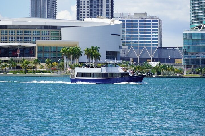 Boat cruises on water with city buildings and palm trees in the background.