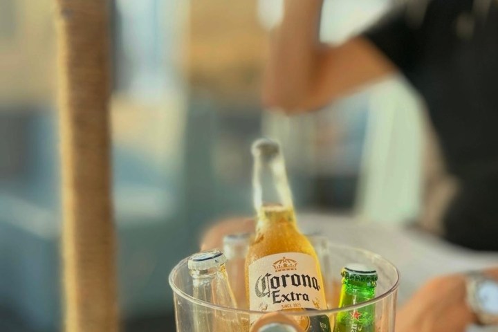 Beer bottles in an ice bucket, person drinking a beer in the background.