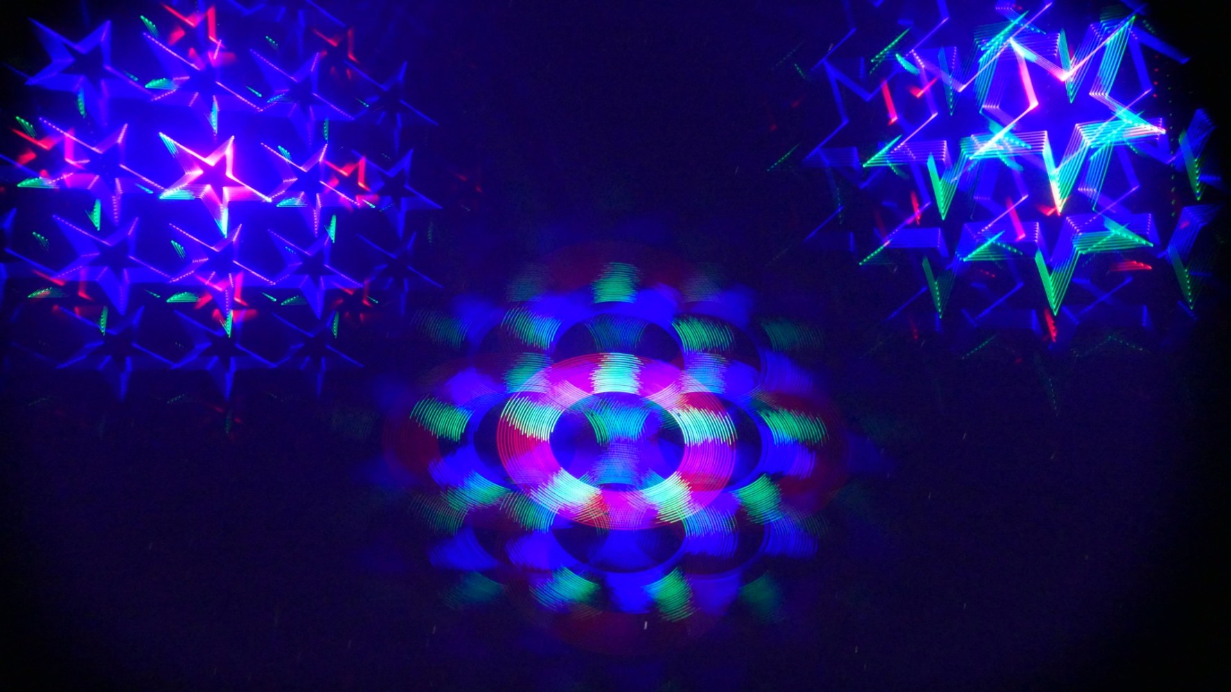 Abstract light pattern with colorful stars and circles on a dark background.