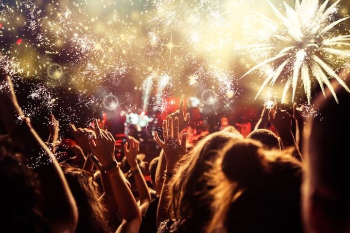 Crowd of people at night with raised hands and fireworks in the sky.