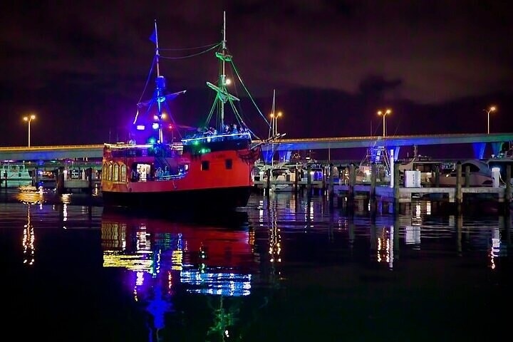 Ship with colorful lights docked at night with reflections on the water.