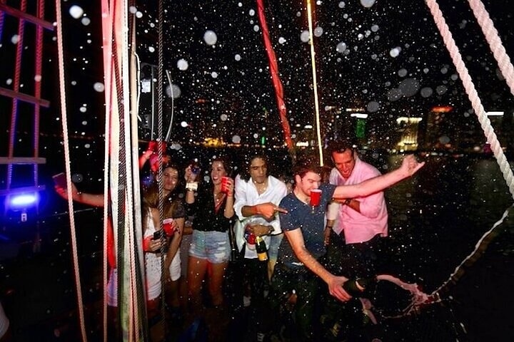 Group of people partying on a boat at night with water splashes.