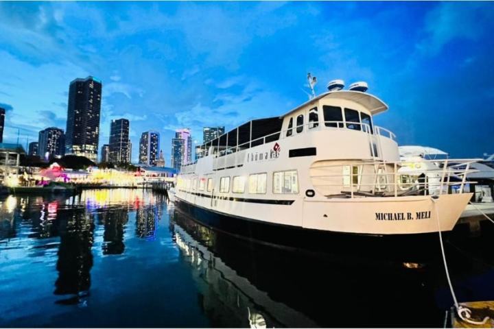Boat docked in a harbor at dusk with city skyline illuminated in the background.