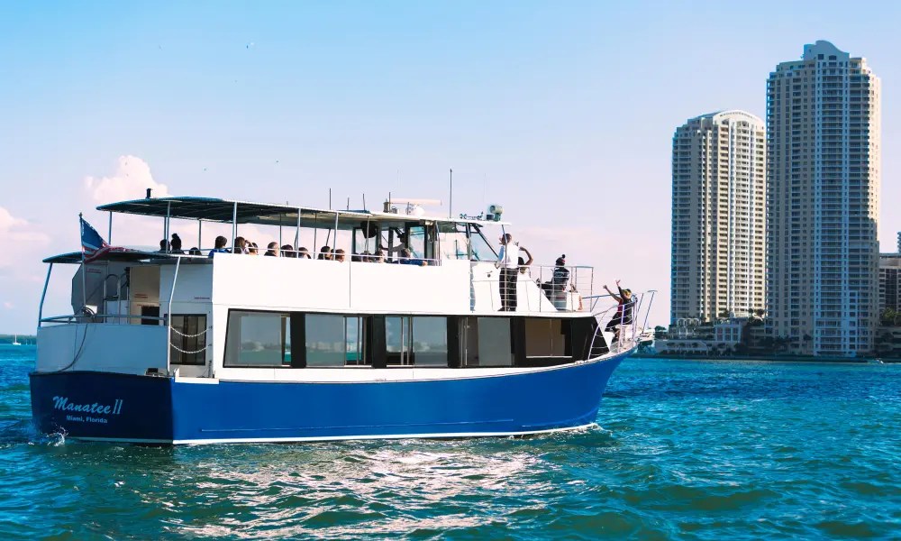 A blue and white boat on the water with people on board, near tall buildings.
