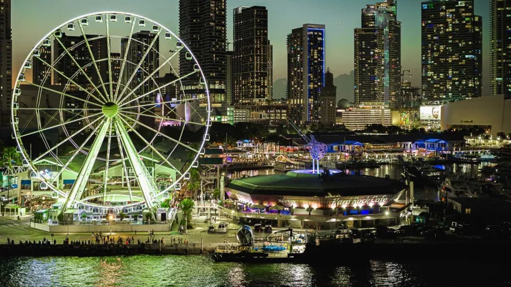 A lit-up Ferris wheel and city skyline at dusk beside a waterfront.