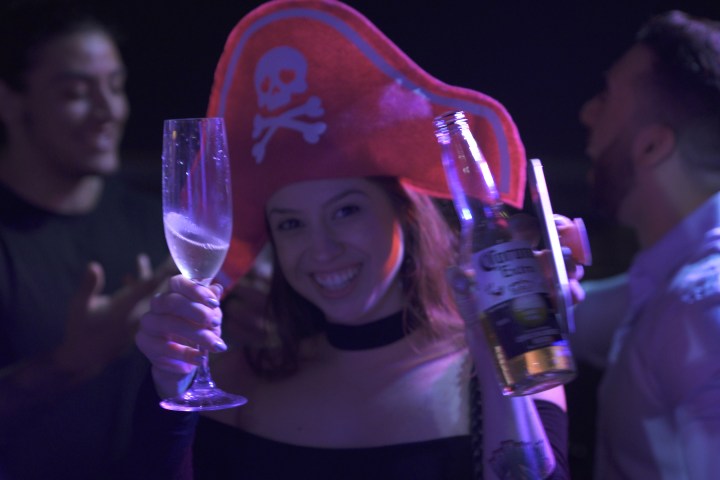 Person in pirate hat holding drinks at lively party with friends.
