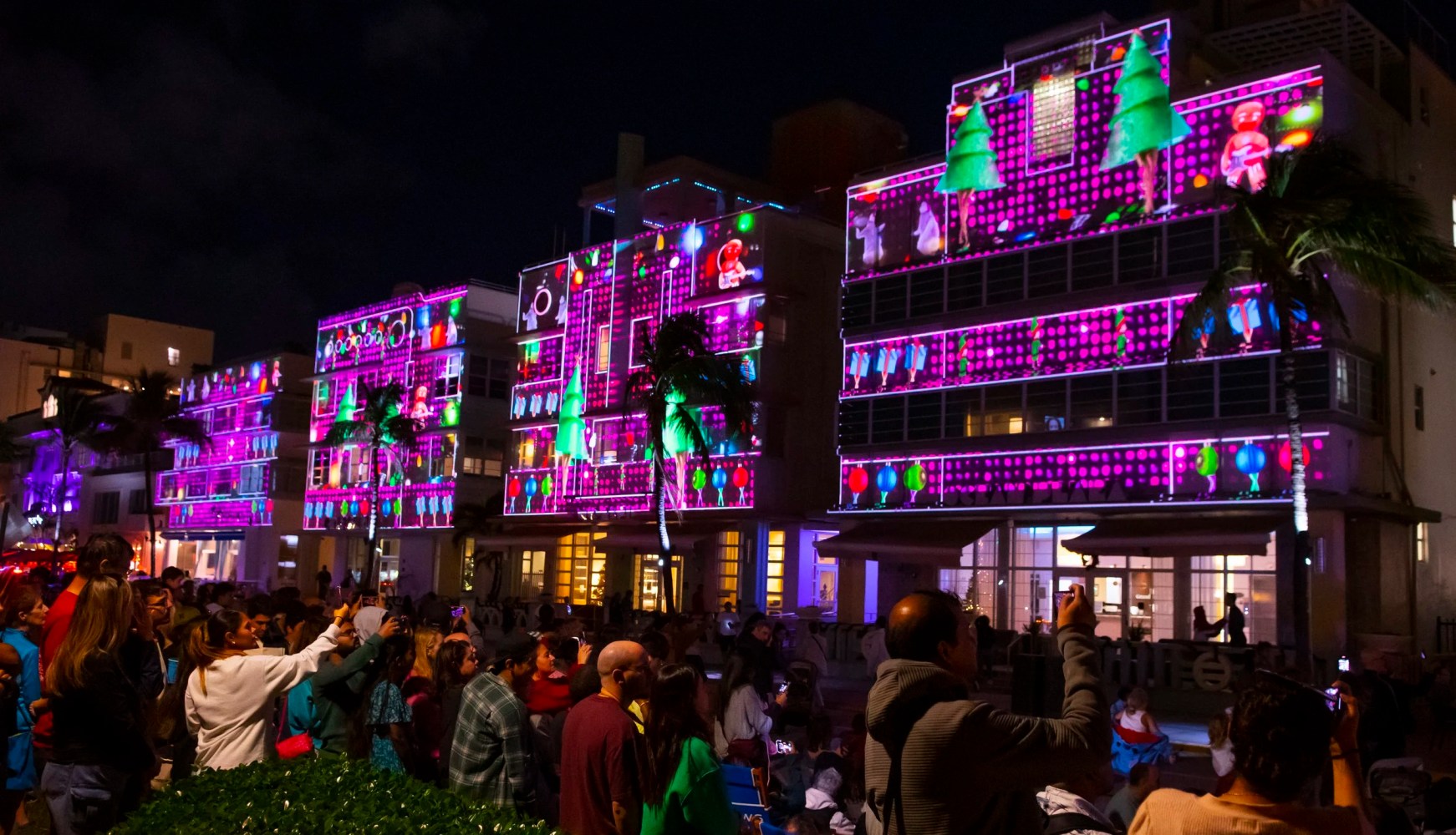 Crowd watching colorful light projections on buildings at night.