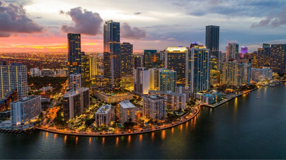 Aerial view of a city skyline at sunset with skyscrapers and waterfront.