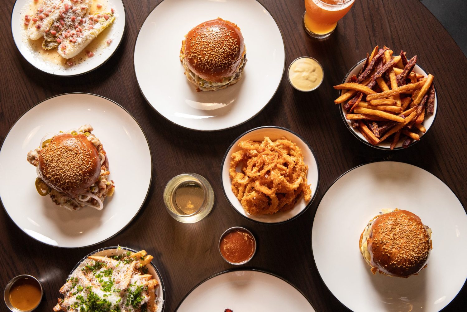 A table with burgers, fries, onion rings, and drinks arranged on white plates.