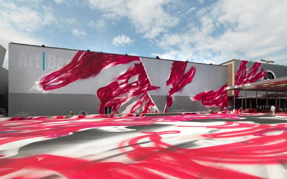 Large mural with red abstract streaks on a building facade against a cloudy sky.