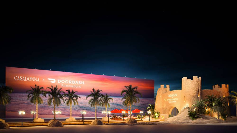 Night scene with palm trees, beach backdrop, and sandcastle with Casadonna and DoorDash logos.