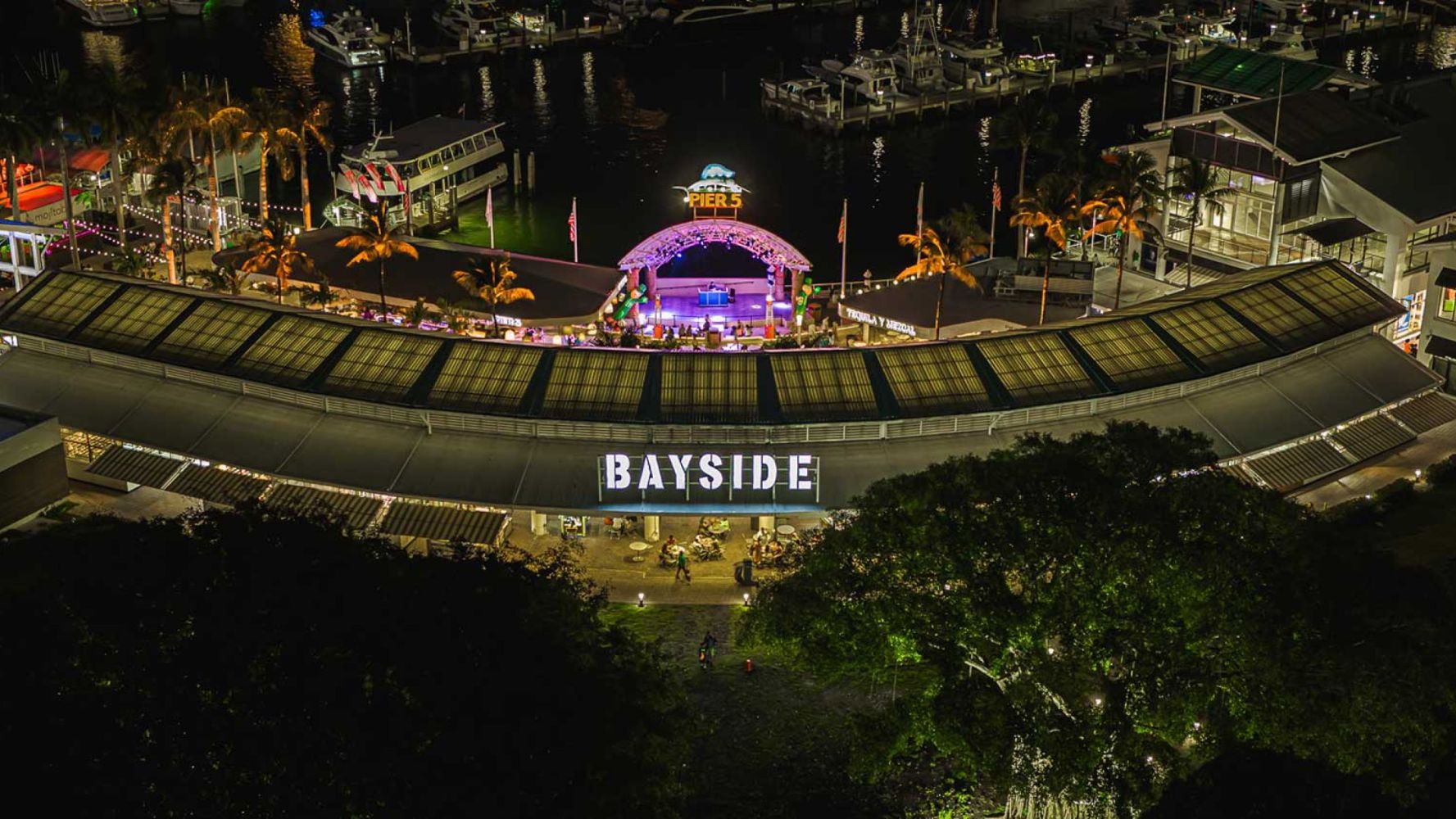 Night view of Bayside Marketplace with illuminated sign and marina backdrop.