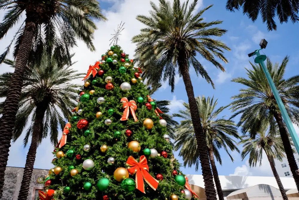 Decorated Christmas tree with red, gold ornaments, surrounded by palm trees under a blue sky.