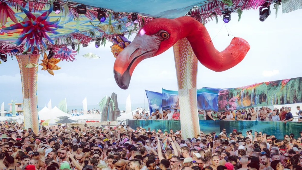 Crowded beach party with large pink flamingo decoration hanging from the ceiling.