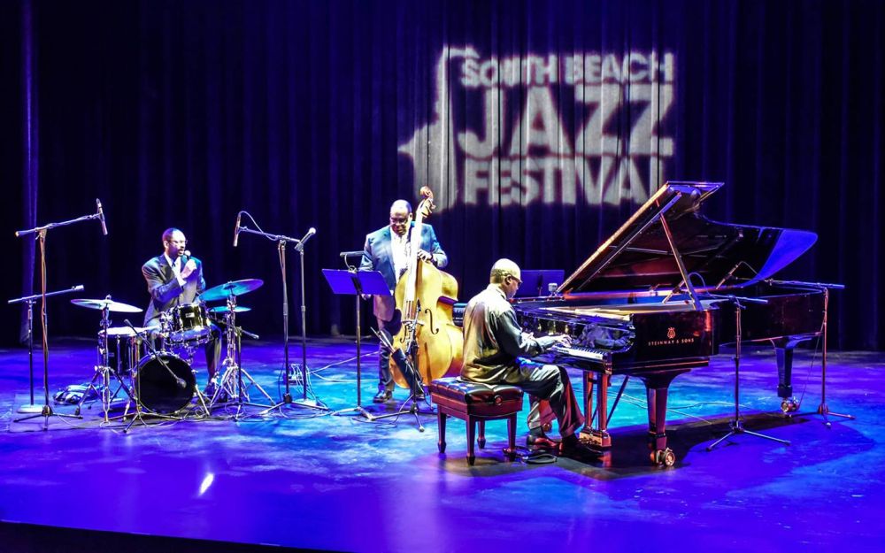 Jazz trio performs on stage with drums, double bass, and piano at South Beach Jazz Festival.