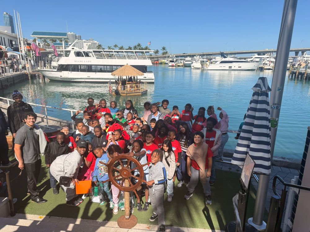 Group of people posing near docks with boats in the background on a sunny day.