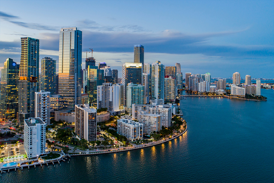 Aerial view of city skyline with high-rise buildings by the waterfront at dusk.