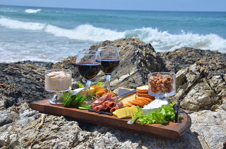 Charcuterie board with wine glasses on rocks by the ocean waves.