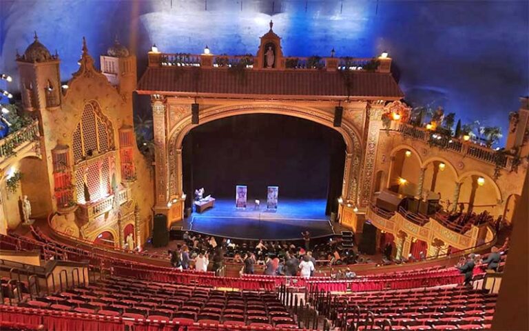 Ornate theater interior with stage and red seats, viewed from balcony.