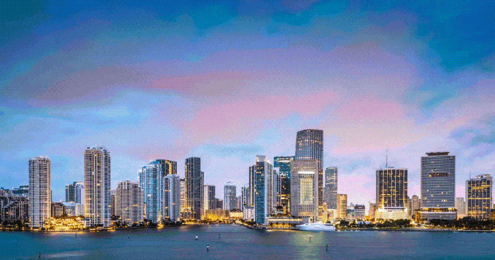 Night view of a city skyline with illuminated skyscrapers and a colorful sky.