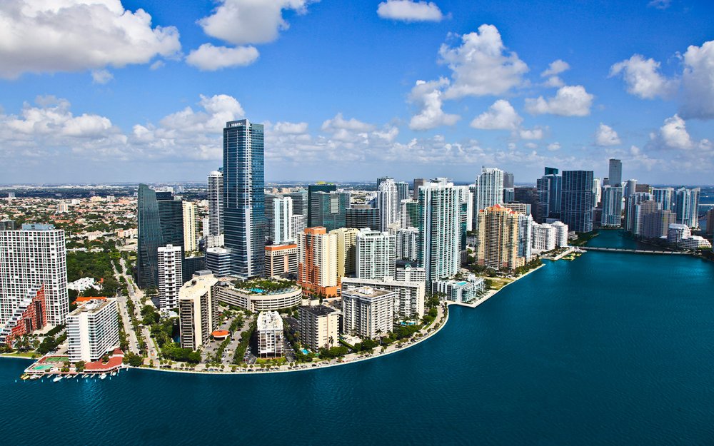 Aerial view of city skyline with tall buildings and waterfront on a sunny day.
