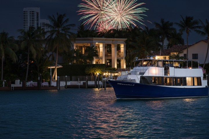Boat on water with fireworks above and buildings in the background at night.