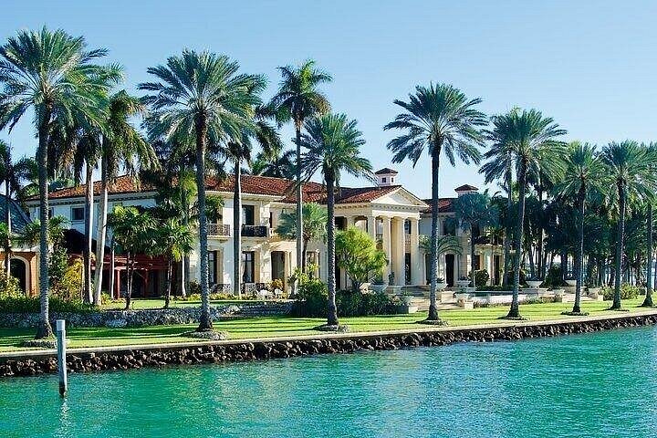 Large mansion with palm trees beside a turquoise waterfront.
