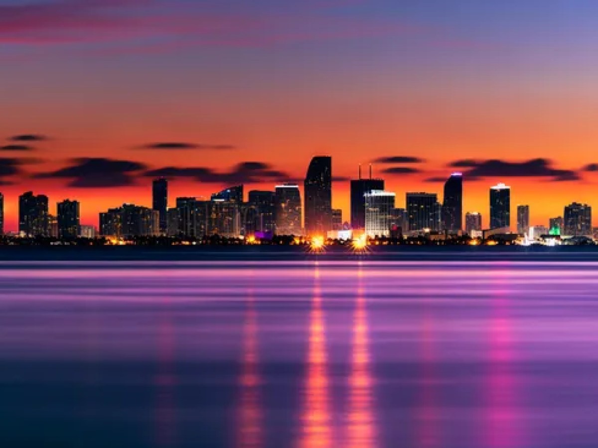 City skyline at sunset with colorful reflections on calm water.