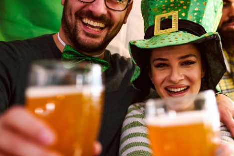 Smiling couple celebrates with beer, wearing festive green attire and hats.