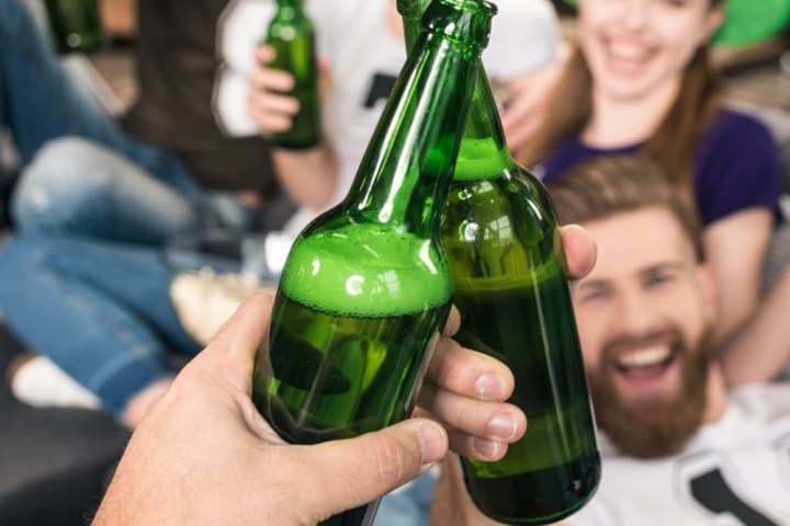 Four people cheering with green beer bottles, two wearing green tall hats.