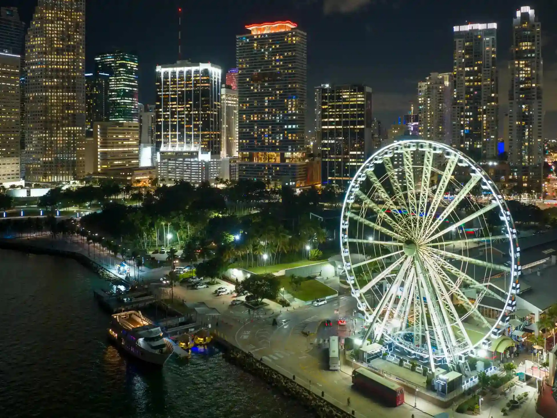 Nighttime cityscape with illuminated Ferris wheel and skyscrapers by the waterfront.