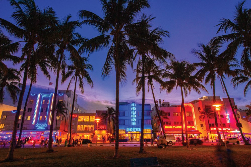 Colorful art deco hotels with neon lights and palm trees at dusk.