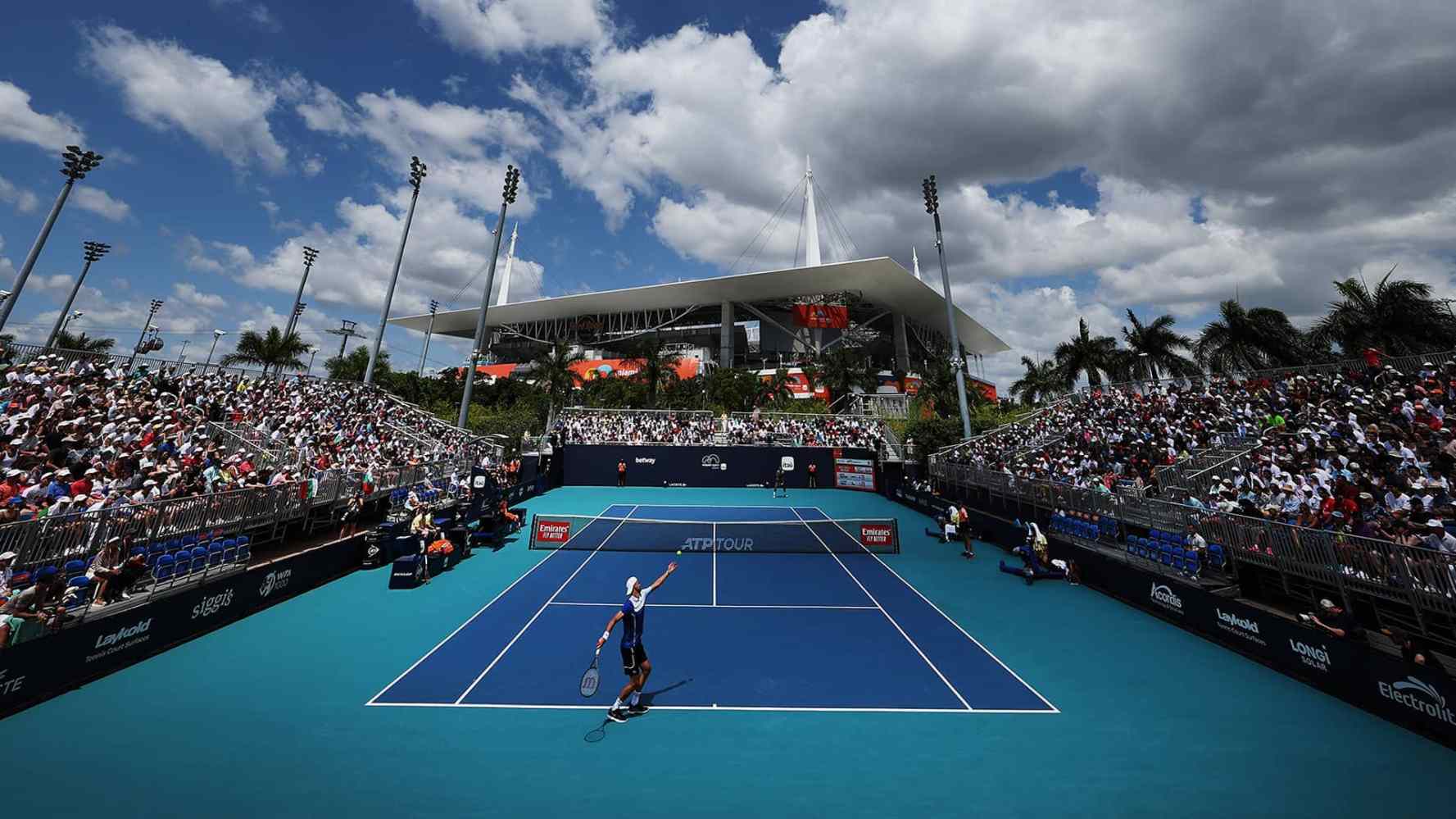 Outdoor tennis match at a stadium with a large crowd and a blue sky.