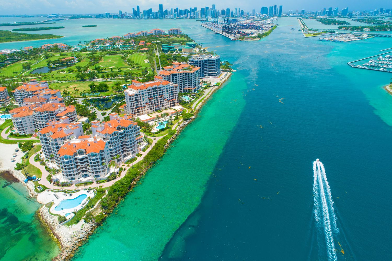 Aerial view of coastal resort buildings with red roofs and boats in clear blue water.