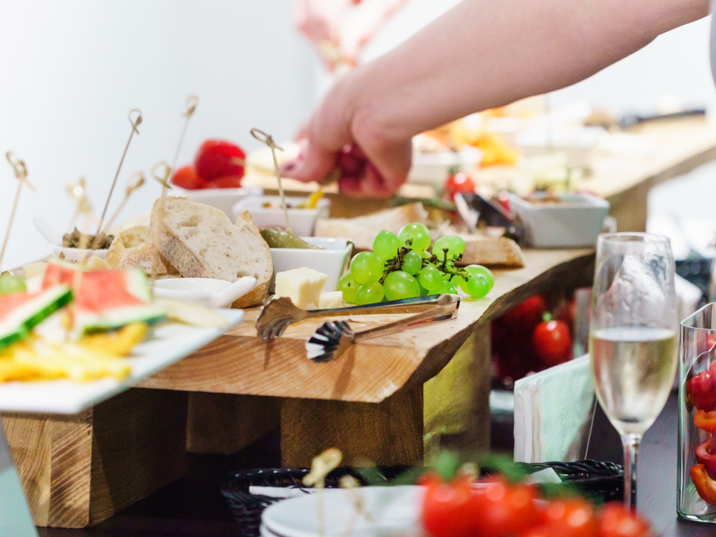 Buffet table with assorted finger foods and a person's hand picking grapes.