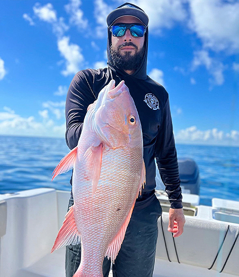 Person holding a large fish on a boat under a blue sky.