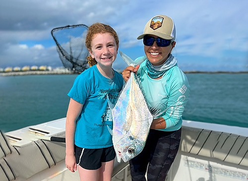 Two people on a boat, one holding a shiny fish, smiling at the camera.