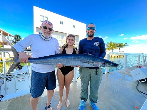 Three people holding a large fish on a dock near the water.