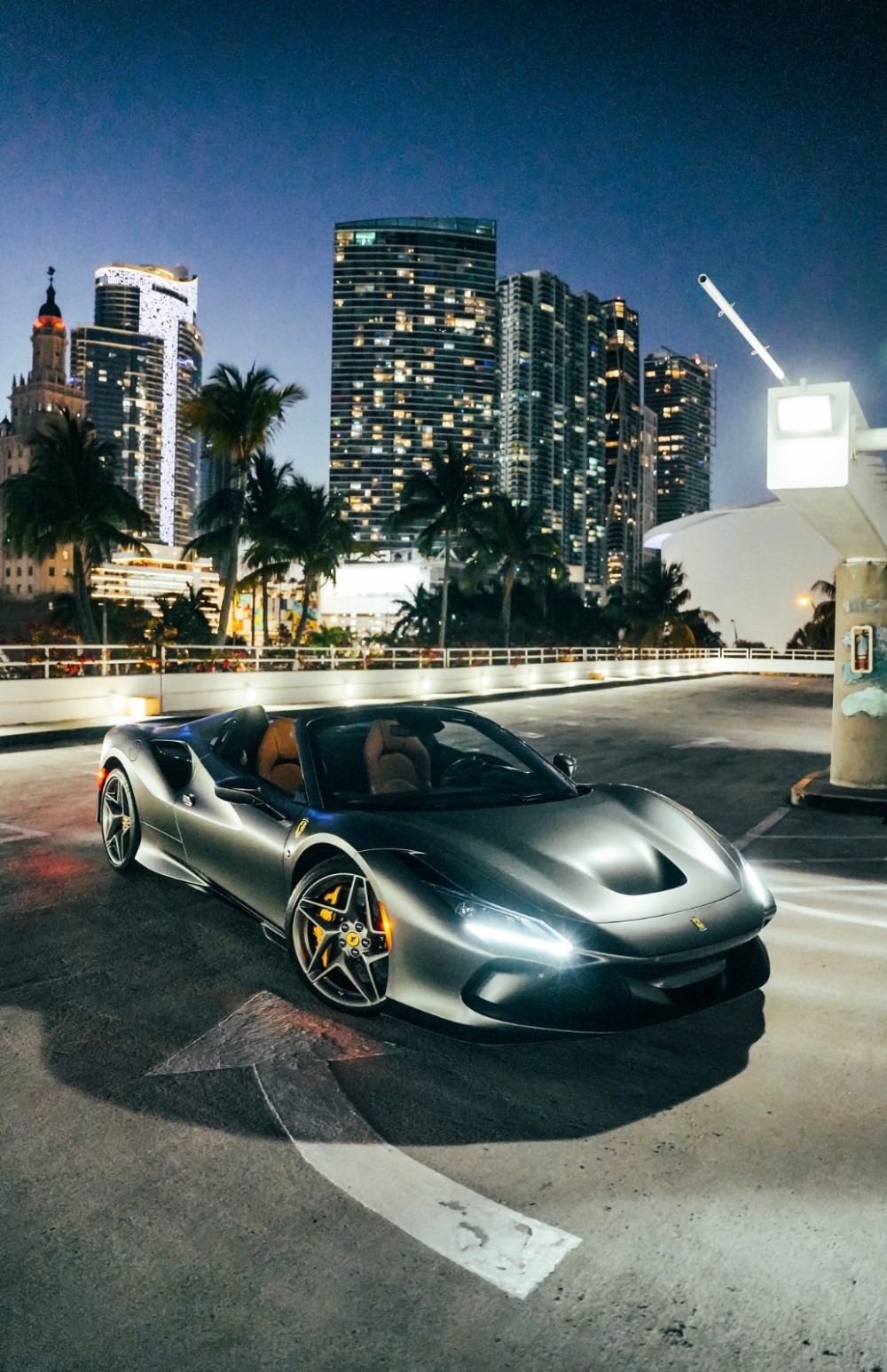 Silver sports car parked on city street at dusk, with tall buildings in the background.