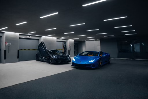 Two luxury cars in a dimly lit garage, one with open scissor doors.